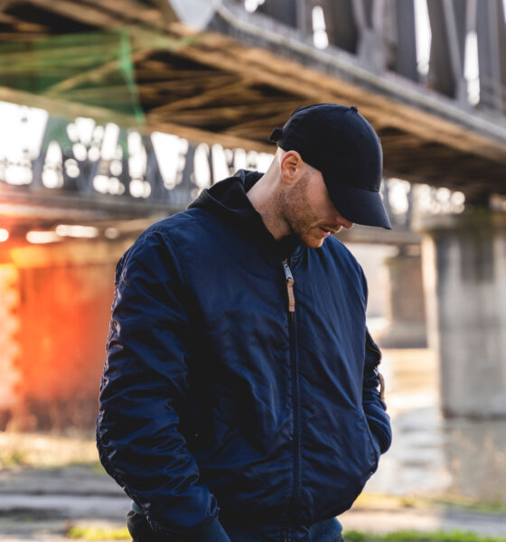 portrait of young rapper posing under a metal bridge in the suburbs